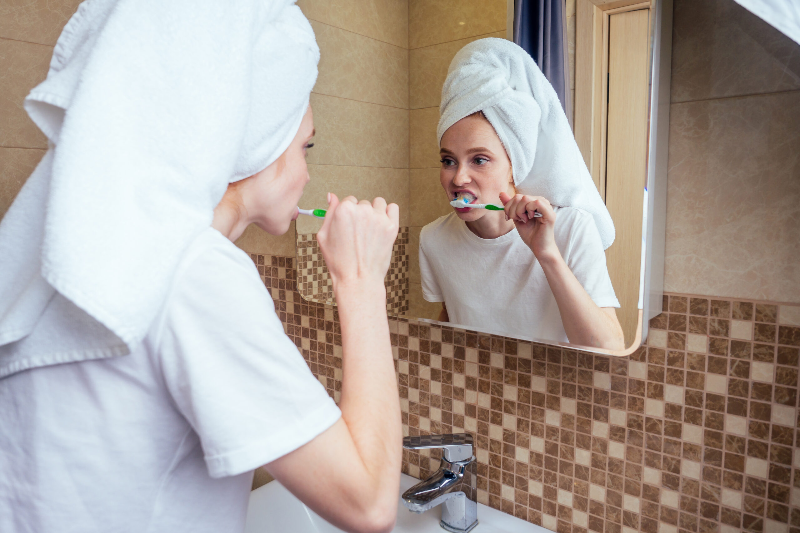 Beautiful woman brushing her teeth in the bathroom after taking a shower before date